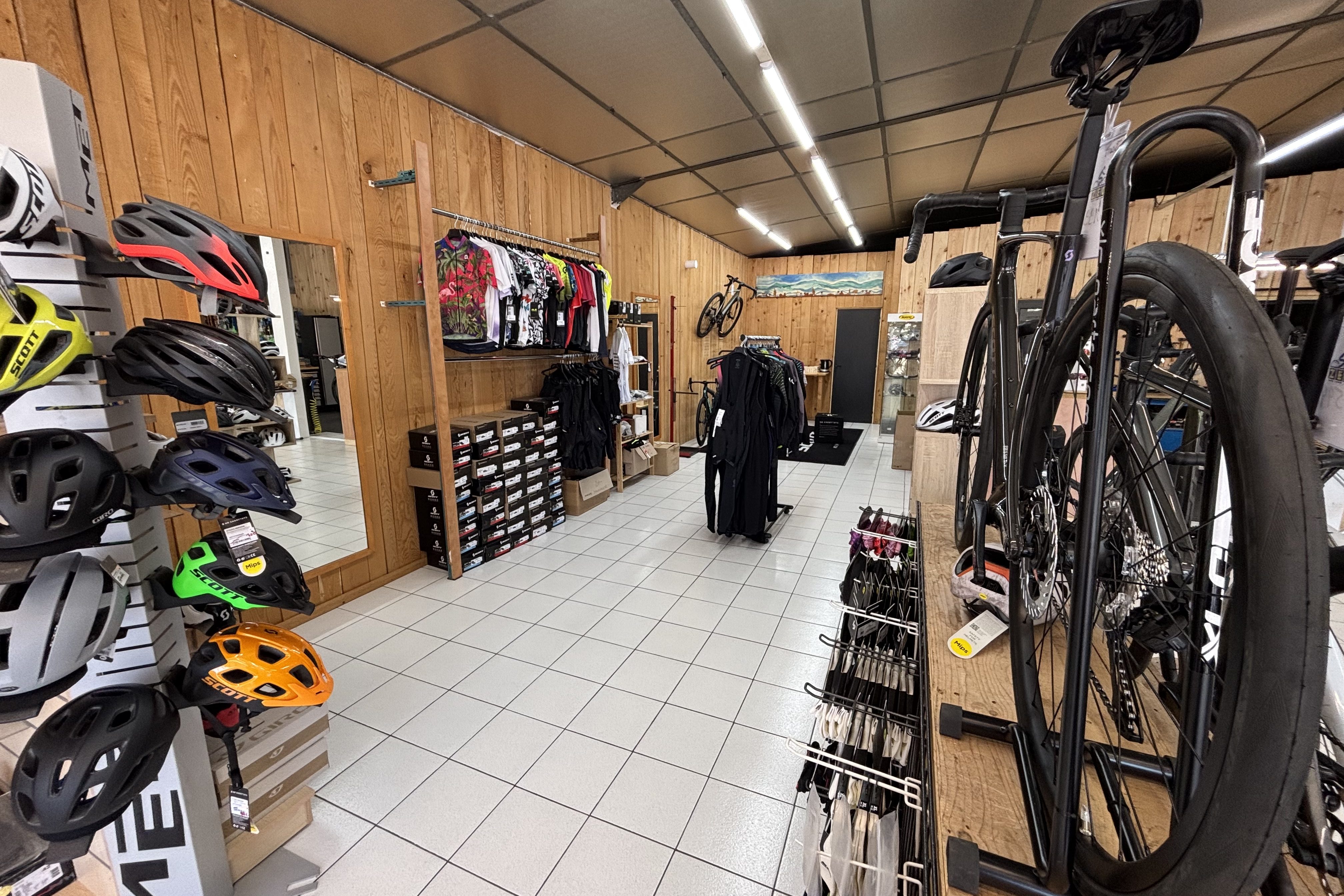 Intérieur d'un magasin de cyclisme avec des casques, des vêtements et des vélos exposés sur des étagères en bois.